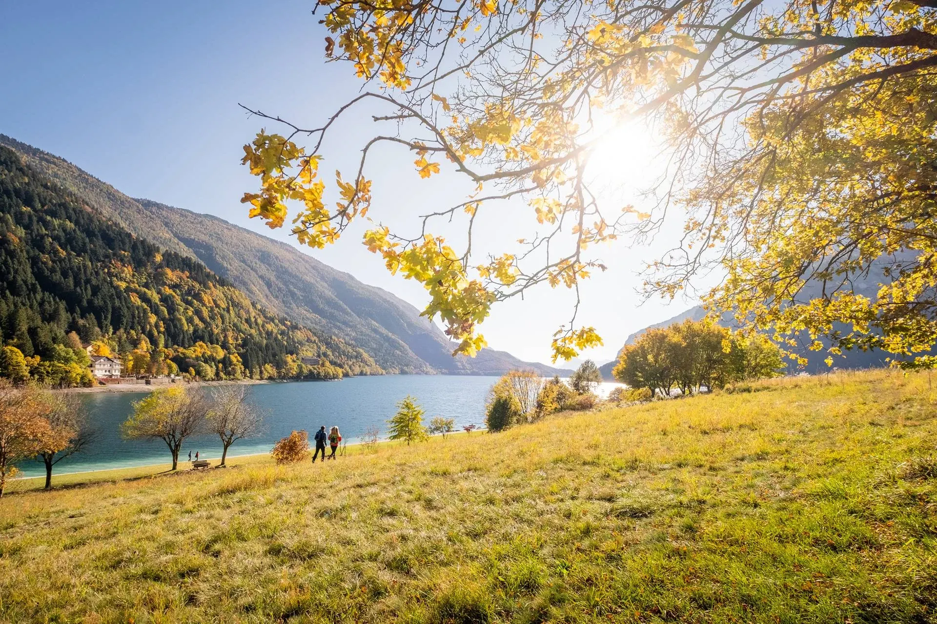 Two people walking along the shore of Lake Molveno in autumn